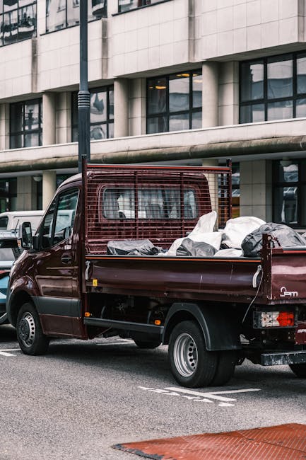 A small burgundy pickup truck parked on an urban street, loaded with a variety of waste materials including white and black rubbish bags, some of which are partially open revealing indeterminate debri